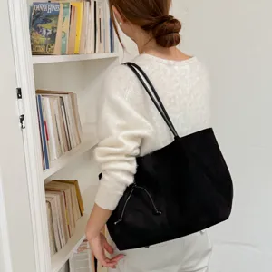 Detailed view of black suede shoulder tote bag with drawstring, styled with casual knitwear.