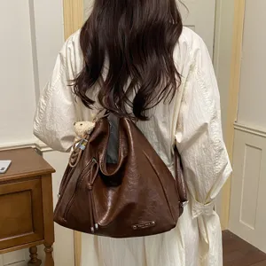 Detail view of brown slouchy leather backpack bag, featuring soft texture and bear charm.