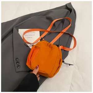 Orange nylon drawstring bucket bag detail view, showing mesh pocket and adjustable strap.