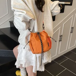 Orange nylon bucket crossbody bag with drawstring closure and mesh side pocket, detail view.