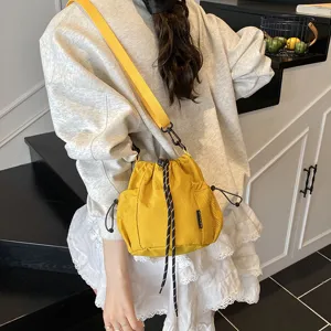 Detailed shot of yellow nylon drawstring bucket cross-body bag with wide strap and side mesh pocket.