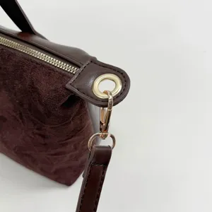 Close-up detail shot of the brown suede handbag showing luxury gold metal hardware and zipper.