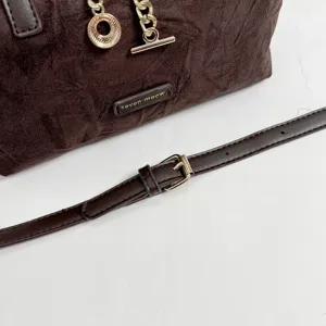 Close-up detail of brown suede handbag with metal chain pendant and adjustable strap.