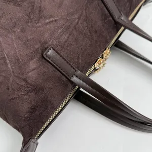 Close up detail of dark brown suede handbag showing zipper, texture and handle craftsmanship.