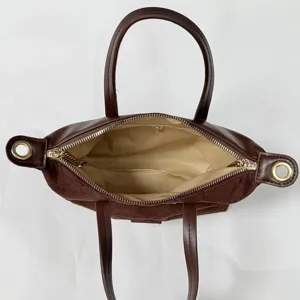 Detailed view of a brown suede top handle handbag featuring gold hardware and zipper.