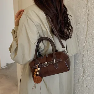 Detailansicht einer retro braunen Wildleder Boston Handtasche mit Anhänger und Gurt.