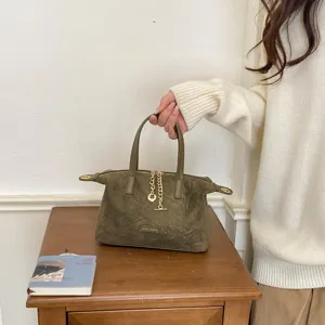 Detailed view of olive green suede handbag with metal chain charm and sturdy top handle.