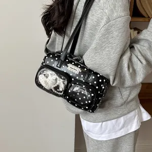 Close-up of black and white polka dot shoulder bag showing transparent front pocket and details.