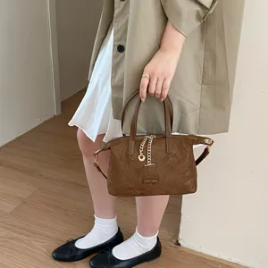 Brown suede handbag detail view, showing vintage design with metal chain and top handle.