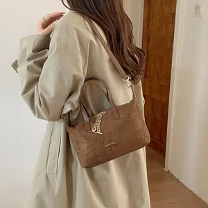 Detail shot of vintage brown suede handbag showcasing exquisite metal chain charm and refined texture.