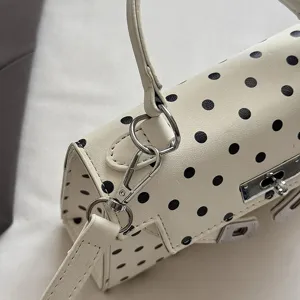Close-up view of white polka dot leather handbag showing metallic lock and strap details.
