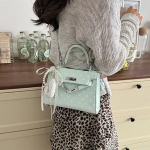 Green polka dot shoulder bag, stylish top handle bag with charm detail, chic design.