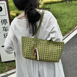 Detailed view of women's green woven tote bag with beaded charm accessory outdoors.
