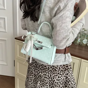 Detail view of light green polka dot shoulder bag with metal lock and cute ribbon heart pendant.