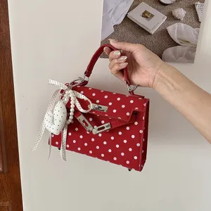 Detailed view of the stylish red polka dot handbag with Kelly design, top handle and charm.