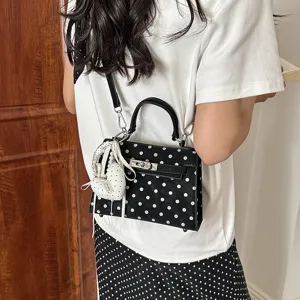 Detail shot of black polka dot Kelly bag with cute heart pendant, worn cross-body elegantly.