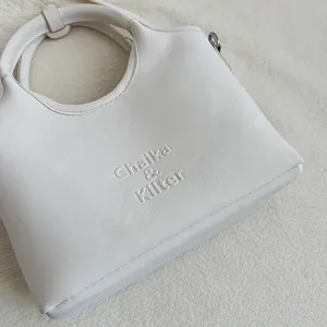 Detailansicht der weissen Leder Eimer Tasche mit gepraegtem Logo, elegante Umhaengetasche.