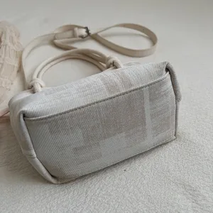 Detailansicht der cremefarbenen Eimer Tasche aus Canvas mit oberen Griffen und verstellbarem Gurt.