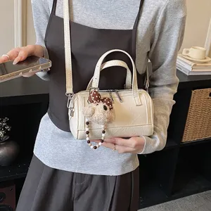 Detailed view of cream white PU boston pillow bag with cute plush bear charm and handle.