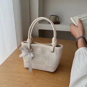 Nahaufnahme der eleganten Beigefarbenen Eimer Tasche mit Knotengriffen und Perlenherzschleife.