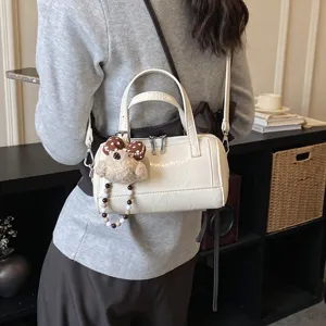 Small white patent leather boston bag with cute bear charm, stylish crossbody shoulder bag detail.