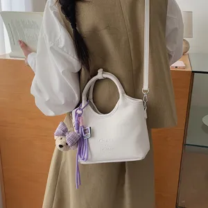 Weisse Leder-Eimer-Tasche Detailansicht mit niedlichem Bärenanhänger und Schulterriemen.
