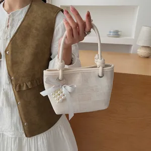 Detailaufnahme der modischen Damen Eimer Tasche in Beige mit Schleife und Perlenanhänger.