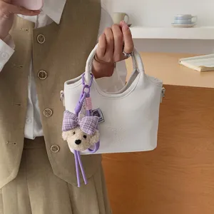 Modische weiße PU-Leder Eimer Tasche für Damen mit süßem Bären-Anhänger und praktischem Griff.