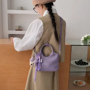 Detailansicht der stylischen violetten Beuteltsche mit süßem Bärenanhänger und feiner Textur.