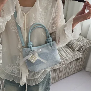Hellblaue Jeans Handtasche Detailansicht mit Perlen Herz Schleife Anhänger und Schultergurt.