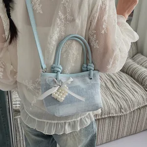 Detailaufnahme einer stylischen hellblauen Jeans-Eimer-Tasche mit Perlenherz-Anhänger.