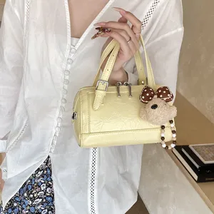 Detail view of a yellow patent Boston handbag with cute bear pendant and metal zipper closure.