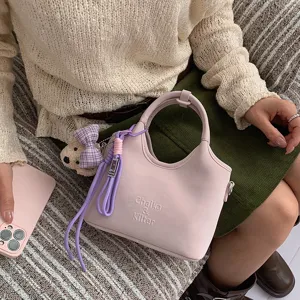 Detailaufnahme der stilvollen rosa Eimer Handtasche mit Bärenanhänger und lila Lanyard.