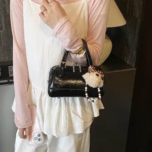 Black patent leather pillow bag with cute plush puppy charm, trendy fashion handbag.
