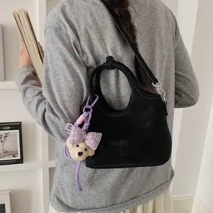 Detailansicht einer schwarzen Eimertasche mit Henkeln, Schultergurt und einem süßen Bärenanhänger.