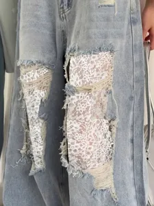 Gros plan sur un jean femme bleu clair déchiré avec de délicats inserts en dentelle blanche.