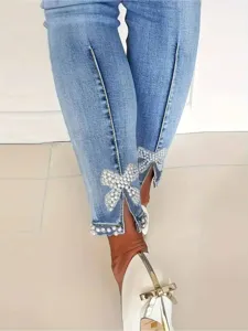 Detail view of women's slim stretch denim jeans featuring pearl bow hem slits and chic style.
