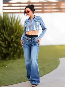 Detailed shot of cropped denim jacket and flared jeans worn by a model in outdoor setting.