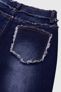 Dettaglio in primo piano di jeans scuri con bordi sfrangiati e tasche posteriori.