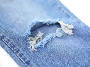 Close up view of distressed light blue denim jeans with ripped knee design and neat stitching.