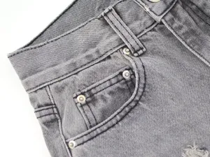 Close-up of stylish gray denim pants showing the front pocket, metallic rivets and texture.