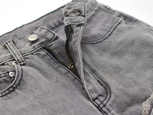 Close-up detail of grey washed denim jeans featuring metal zipper fly and classic pocket design.