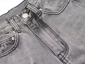 Grey washed denim jeans detail shot, featuring classic button fly and pockets for women style.