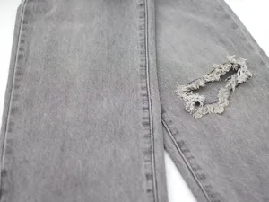 Grey denim jeans detail shot showing distressed ripped knee and fine stitching craftsmanship.