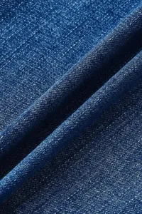 Close up view of dark blue denim fabric with natural folds and fine diagonal texture detail.