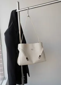 Minimalist faux leather shoulder bag detail with elegant metal clasp and side strap accents.