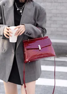 Detail view of a stylish red crocodile pattern handbag with metal lock and shoulder strap.