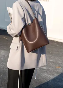 Detail shot of brown leather bucket bag worn with gray blazer in outdoor street style.