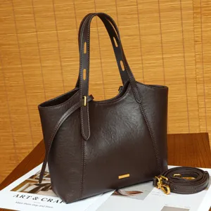 Dark brown leather tote bag detail showing premium texture, dual handles and metal accent.