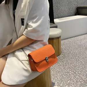 Detail view of the orange litchi pattern leather crossbody bag with chic metal chain and lock.